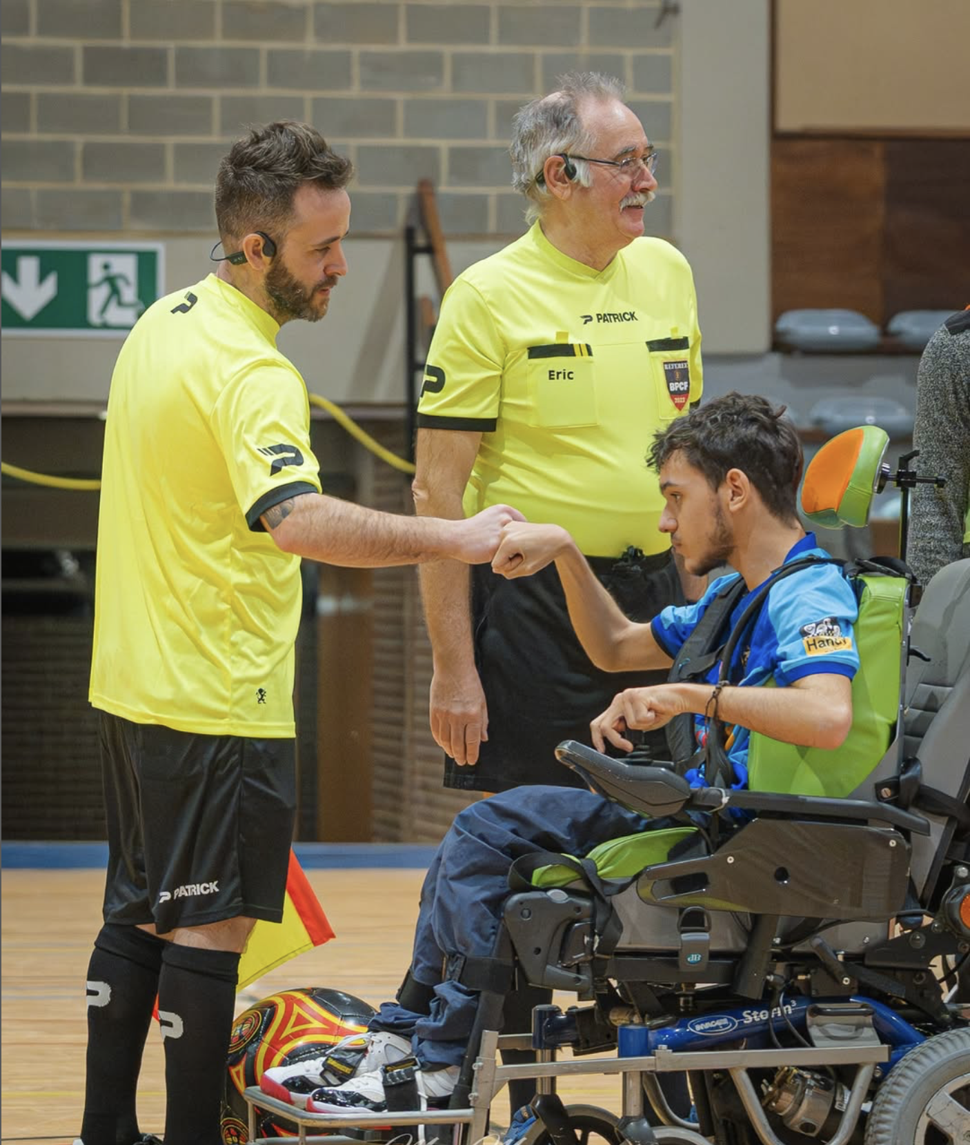 A soccer player with a physical disability participates in the sport on a wooden court, utilizing a wheelchair-designed fo...